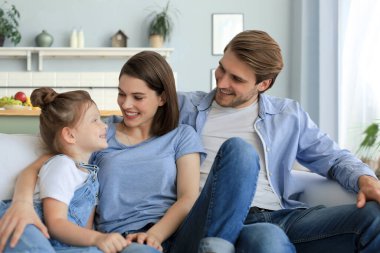 Hafta sonları evde dinlenirken, kanepede birlikte oturan gülümseyen küçük bir kızı olan olumlu, arkadaş canlısı ebeveynler..