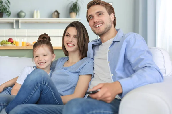 Gelukkig gezin met kind zitten op de bank tv kijken, jonge ouders omarmen dochter ontspannen op de bank samen. — Stockfoto