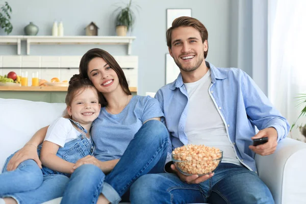 Gelukkig gezin met kind zitten op de bank tv kijken en het eten van popcorn. — Stockfoto
