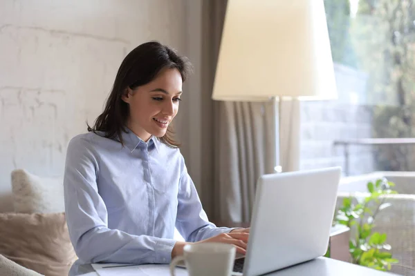 Jolie femme souriante assise à table, regardant l'écran de l'ordinateur portable. Heureux entrepreneur lire message email avec de bonnes nouvelles, bavarder avec les clients en ligne. — Photo