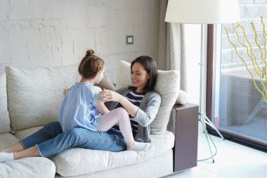 Sevimli küçük kız gülüyor kanepede annesiyle oynuyor, mutlu anne rahatlıyor komik küçük kız çocukla eğleniyor birlikte oturma odasında eğleniyor.