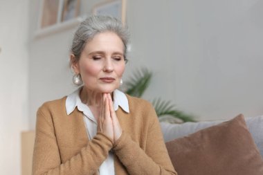 Orta yaşlı bir kadın dua ediyor, gözleri açık, bakıyor, en iyisini umuyor, af diliyor.