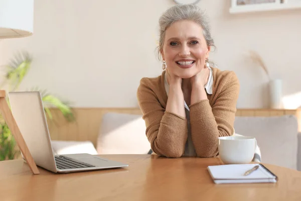Orta Yaşlı Bir Kadın Dizüstü Bilgisayarla Masada Oturuyor Gülümseyen Kameraya — Stok fotoğraf