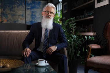 Modern ofisinde koltukta oturup iş kavramını düşünen düşünceli, kendine güvenen yakışıklı iş adamı. Kahve molası