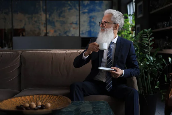 英俊而成熟的男人拿着咖啡杯坐在办公室的沙发上 咖啡休息时间 — 图库照片