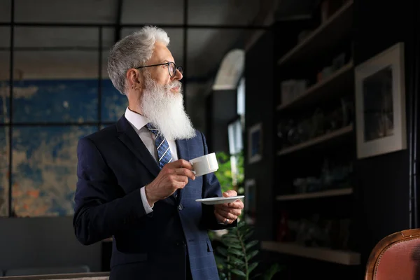 新的工作日开始了 喝一杯咖啡 英俊而成熟的男人拿着咖啡杯站在他现代的办公室里 — 图库照片