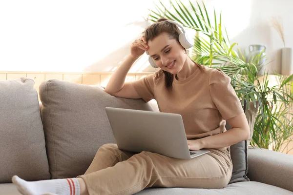 Smilende Ung Kvinne Med Hodetelefoner Laptop Sofaen – stockfoto