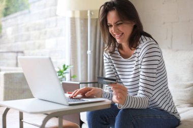 Oturma odasında kredi kartı ve laptop kullanarak mutlu bir esmer.