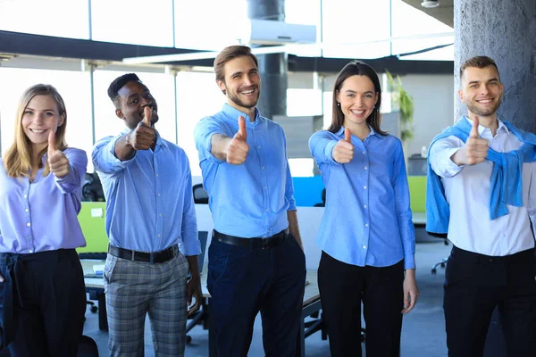 Feliz gente de negocios de pie en la oficina mostrando el pulgar hacia arriba. — Foto de Stock