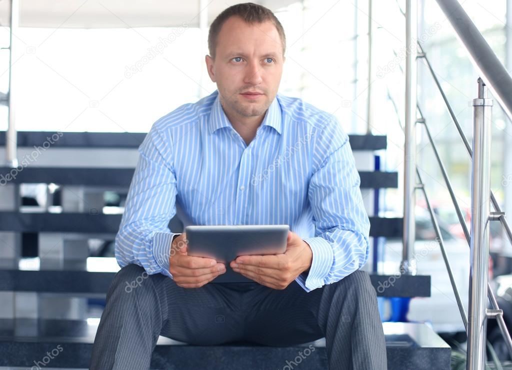 Businessman sitting on stairs with electronic tablet