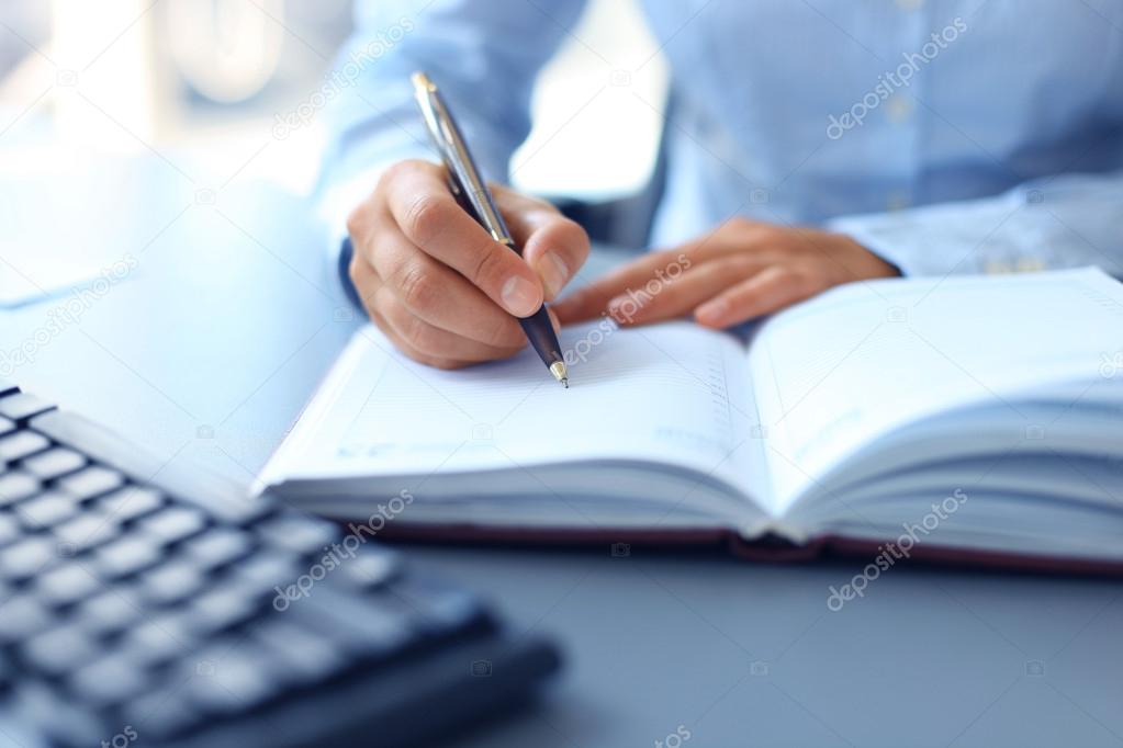 Businessman writes in a notebook while sitting at a desk