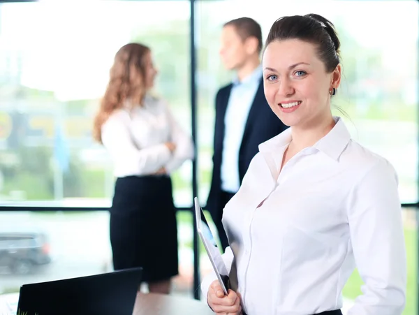 Business woman standing in foreground with a tablet in her hands — Stock Photo, Image