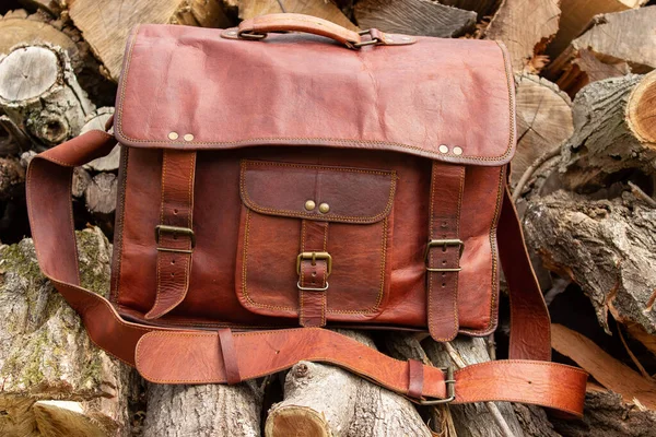 Vintage handmade leather briefcase bag sitting on wood pile outdoors ready for adventure journey