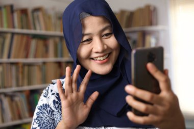 Asyalı Müslüman kadının akıllı telefon kullandığı bir fotoğraf. İnternette iletişim kurarken mutlu gülümseme hareketi, video çağrısı, seçici odaklanma 