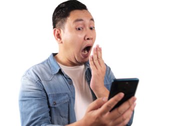 Çekici Asyalı genç adam telefonunda mesajlaşan mesajları okuyor, şaşırmış yüz ifadesi.