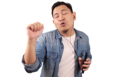 Akıllı telefonuyla kulaklıkla müzik dinlerken mutlu Asyalı genç adam dans ediyor.