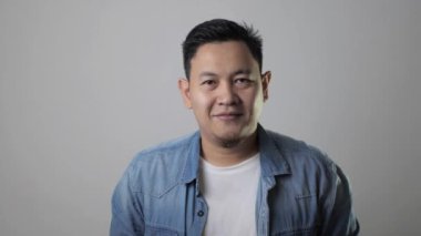 Kameraya gülümseyen başarılı Asyalı genç adam. Gri arkaplan karşısında kendine güveni tam, pozitif bir insan.