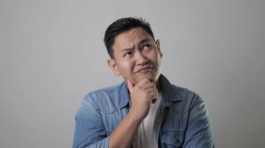 Genç Asyalı adam düşünmekten ve bakmaktan mutlu görünüyordu, iyi bir fikri vardı. Gri duvarlı yarım vücut portresi kopyalama alanı