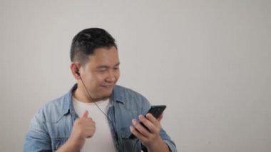 Akıllı telefonuyla kulaklıkla müzik dinleyen neşeli Asyalı genç adam.