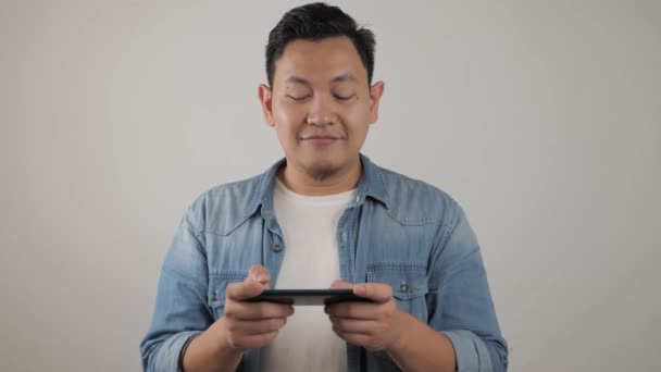 Retrato de un joven asiático guapo jugando juegos en la tableta de teléfono inteligente — Vídeo de stock