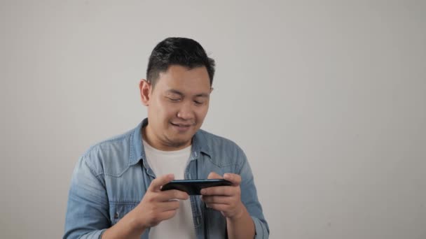 一个年轻英俊的亚洲男人用平板智能手机玩游戏的肖像 — 图库视频影像