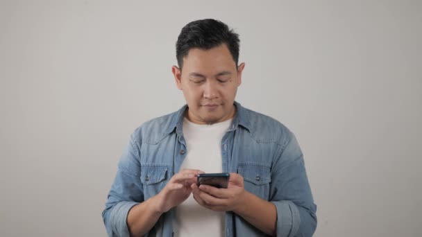 Attraktiver lustiger junger asiatischer Mann liest SMS-Chats auf seinem Handy und lächelt glücklich lachend — Stockvideo