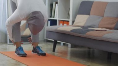 Asyalı Müslüman kadın tesettür takıyor evde egzersiz yapıyor, yeni normal yaşam tarzında sağlıklı ve formda kalıyor, evde egzersiz yapıyor, bacaklarını esnetiyor.