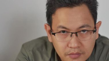 Gözlüklü, kameraya bakıp gülümseyen Asyalı genç adamın portresi.