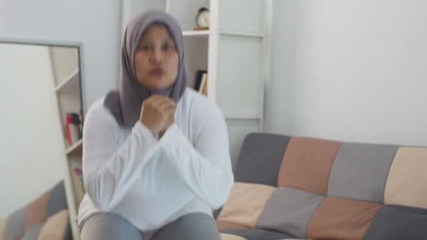 ラップトップでオンラインビデオの指示を見ている間に自宅で運動をするヒジャーブを身に着けているアジアのイスラム教徒の女性 屋内ホームワークアウトの概念 新しい通常のライフスタイルに健康を維持 スクワット — ストック動画