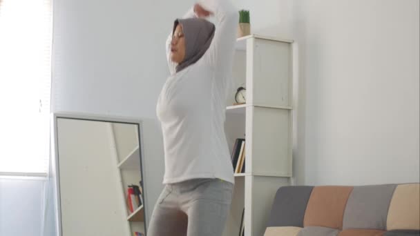 ラップトップでオンラインビデオの指示を見ている間に自宅で運動をするヒジャーブを身に着けているアジアのイスラム教徒の女性 屋内ホームワークアウトの概念 新しい通常のライフスタイルに健康を維持 ジャンプジャック — ストック動画