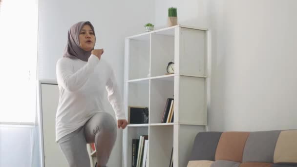 ラップトップ 屋内ホームワークアウトのコンセプトでオンラインビデオ命令を見ている間 自宅で運動をするヒジャーブを身に着けているアジアのイスラム教徒の女性は 所定の位置に実行され 新しい通常のライフスタイルに健康を維持 — ストック動画