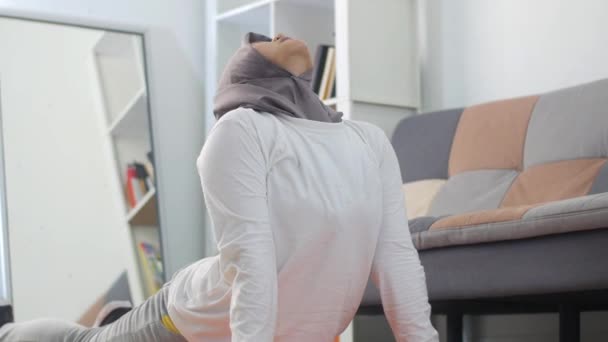 ヒジャーブを身に着けているアジアのイスラム教徒の女性は 自宅で運動をした後 彼女の腕を伸ばし 健康を維持し 新しい通常の生活の中でフィット 屋内ホームワークアウトの概念は ストレッチ — ストック動画