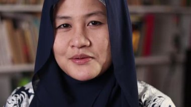 Genç Asyalı Müslüman kadın kütüphanede dikilirken kameraya konuşuyor, iş adamı merkez ofisten video konferansı yapıyor.