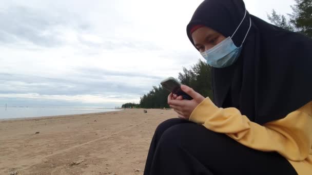 Muzułmanka Ubrana Hidżab Maskę Ochronną Pomocą Smartfona Siedząc Plaży Podczas — Wideo stockowe
