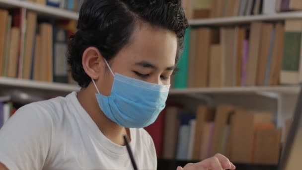 Asian boy student wearing protective mask learning studying online with laptop computer in library, school from home concept — Stock Video