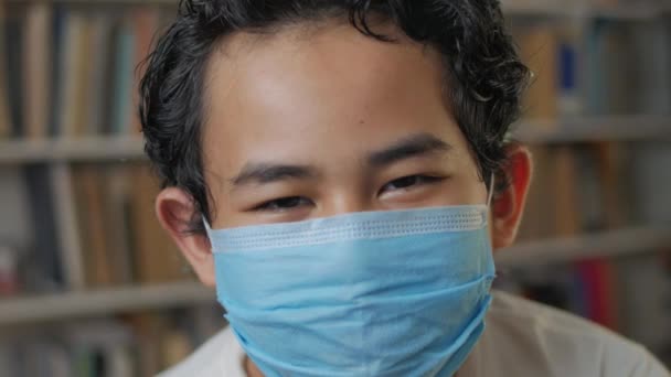 Portret van jonge Aziatische student jongen met beschermende gezichtsmasker in de bibliotheek, nieuw normaal tijdens covid-19 coronavirus pandemy concept — Stockvideo