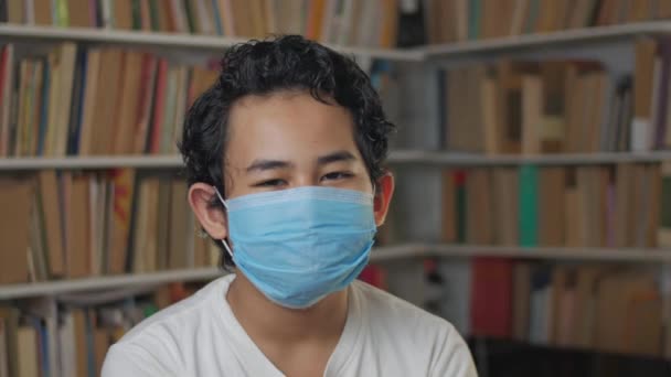 亚洲年轻男生在图书馆戴防护面罩的肖像- -在covid-19冠状体潘水画概念中的新常态 — 图库视频影像