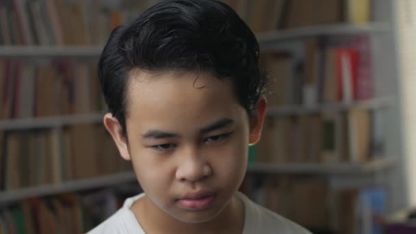 การแสดงออกที่น่าเศร้าของเด็กชายเอเชีย พื้นหลังห้องสมุดเปลือกหนังสือ — วีดีโอสต็อก