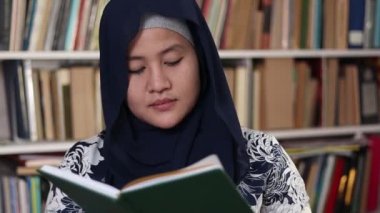 Kütüphanede kitap okuyan mutlu Asyalı Müslüman kadın, eğitim sahnesi