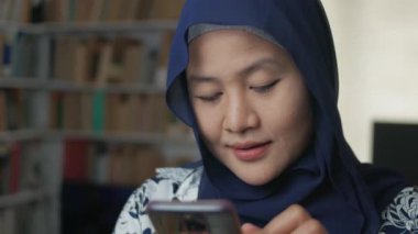 Asyalı Müslüman kadın telefon edip gülümsüyor. Mutlu hissediyorum. Kadın akıllı telefonuyla iletişim kuruyor.