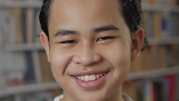 Feliz estudiante asiático alegre sonriendo a la cámara, niño aprendiendo en la biblioteca, retrato de cerca — Vídeo de stock