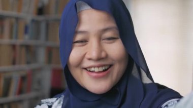 Mutlu, güzel Asyalı Müslüman kadın kameraya el sallıyor, konuşuyor, video çağrısı yapıyor.