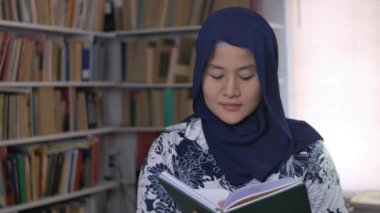 Kütüphanede kitap okuyan mutlu Asyalı Müslüman kadın, eğitim sahnesi, kütüphanede kız öğrenci öğrenimi 