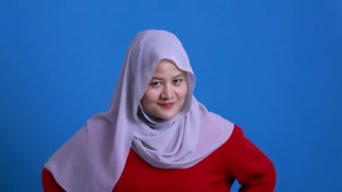 Güzel Asyalı Müslüman kadın tesettürlü düşünüyor, gülümsüyor ve kameraya işaret ediyor.