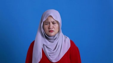 Başörtüsü takan Asyalı Müslüman kadının portresi reddedişini ya da inkar edişini gösteriyor, omuz silkme, ne bileyim, kırmızı arka plana karşı bir ifade.