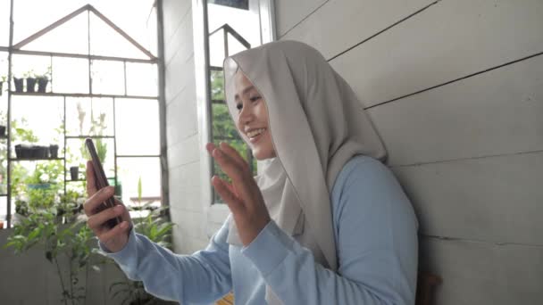 Krásná asijské muslim dáma dělá selfie portrét na telefonu nebo dělat videohovor zatímco sedí mimo svůj domov, šťastný úsměv veselý výraz — Stock video