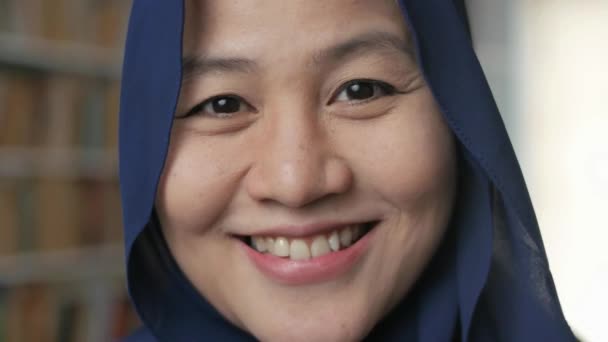 Счастливая красивая азиатская мусульманка в хиджабе, улыбающаяся в камеру, студентка в библиотеке — стоковое видео