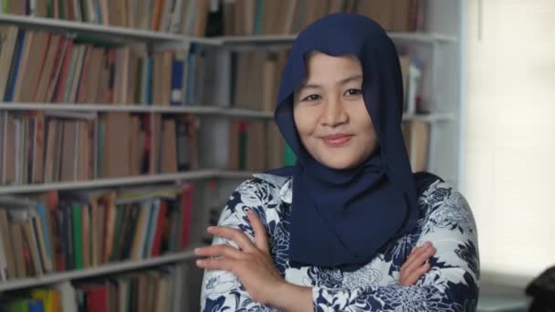 Ritratto di allegra bibliotecaria musulmana asiatica vestita in hijab, che guarda la macchina fotografica e sorride al gesto di fiducia incrociata delle braccia — Video Stock