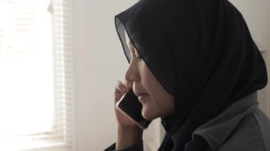 Mutlu Asyalı Müslüman kadın tesettürlü telefonda konuşuyor, iyi haberler iletişim konsepti, gülen yüz, kenar görüş