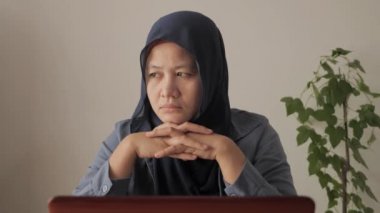 Asyalı Müslüman kadının portresi dizüstü bilgisayarı üzerinde çalışırken düşüncelere dalmak, hüzünlü duygu ifadesi